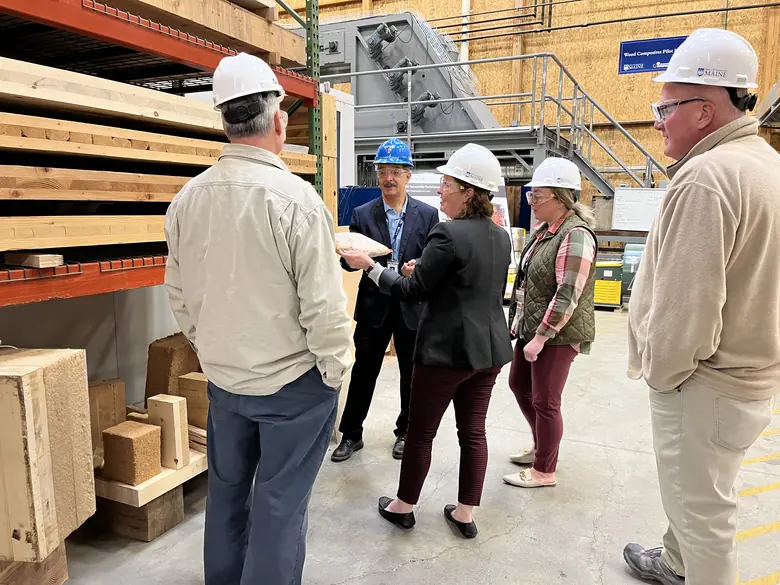 Visitors in hard hats beside timber stock in a University of Maine research lab, 2023