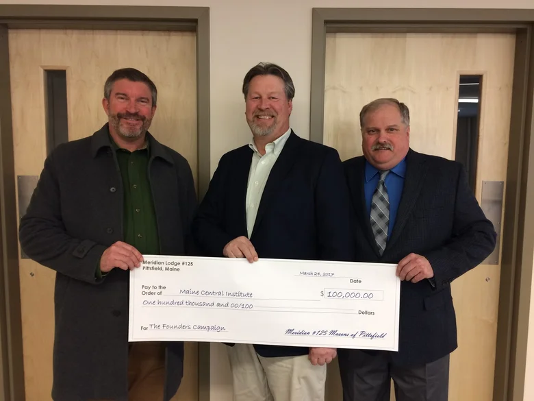Three men stand together holding a large presentation check, 2017
